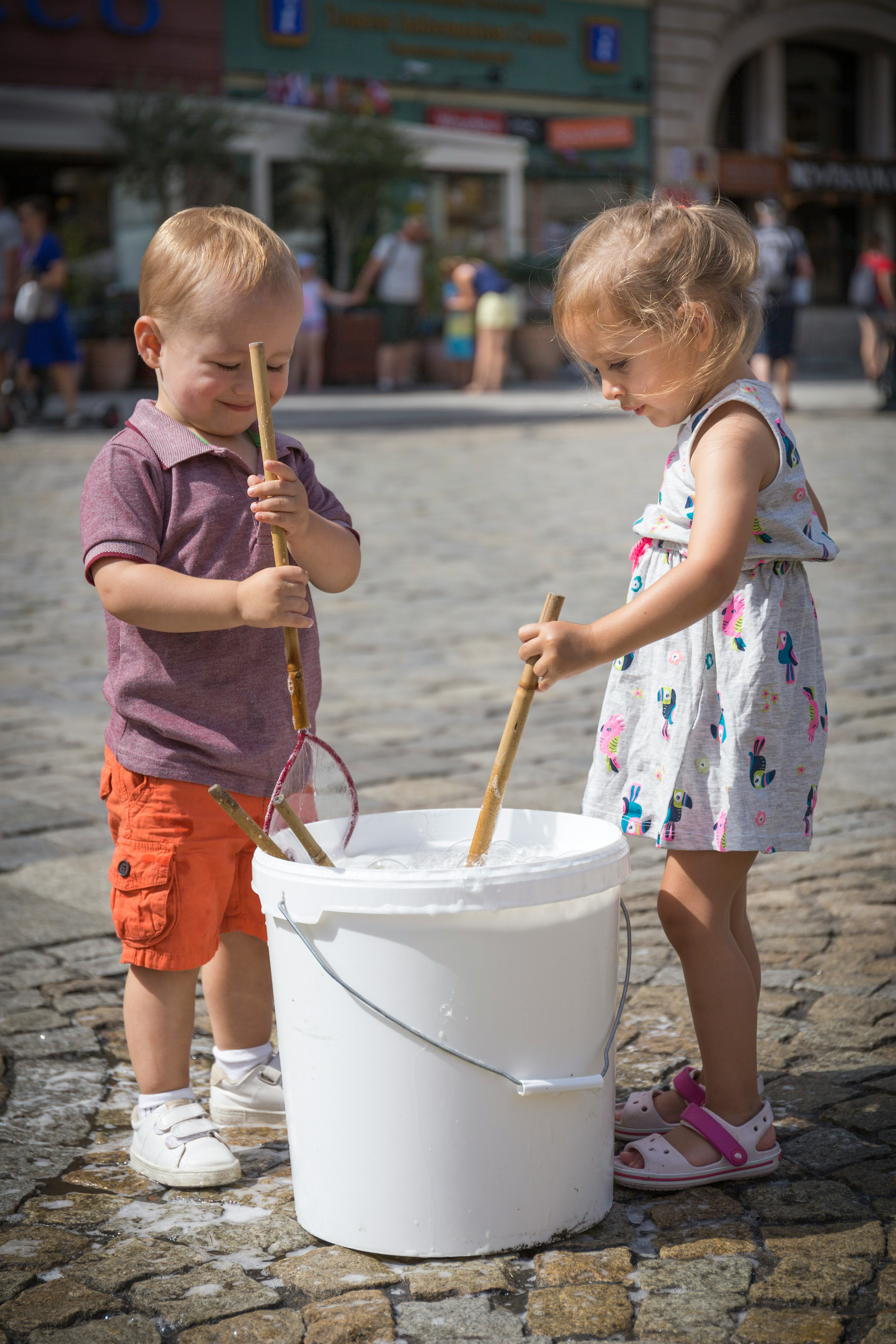 girl in pink and white floral dress holding white plastic bucket