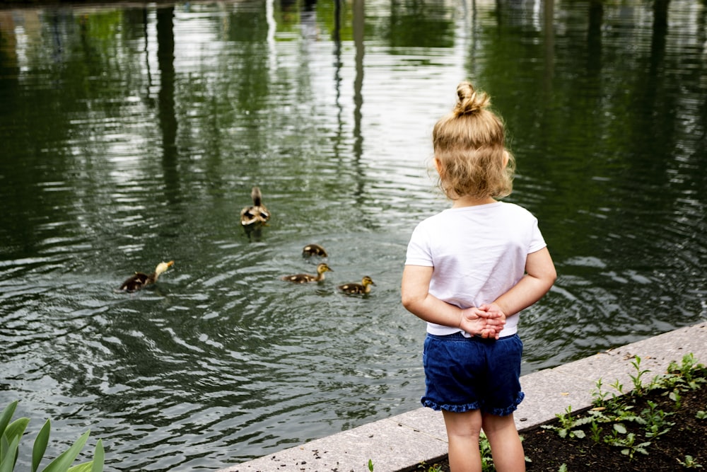 girl in white t-shirt and blue shorts standing on concrete dock with brown and black