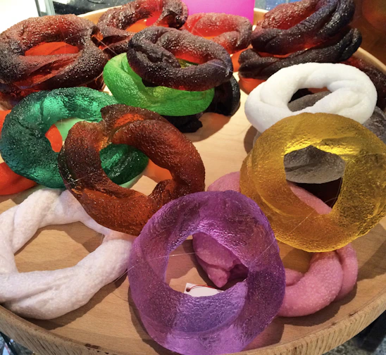 A collection of colorful artificial gemstone rings displayed on a wooden tray.