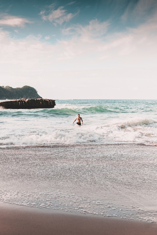 man surfing on sea waves during daytime in Cathedral Cove New Zealand