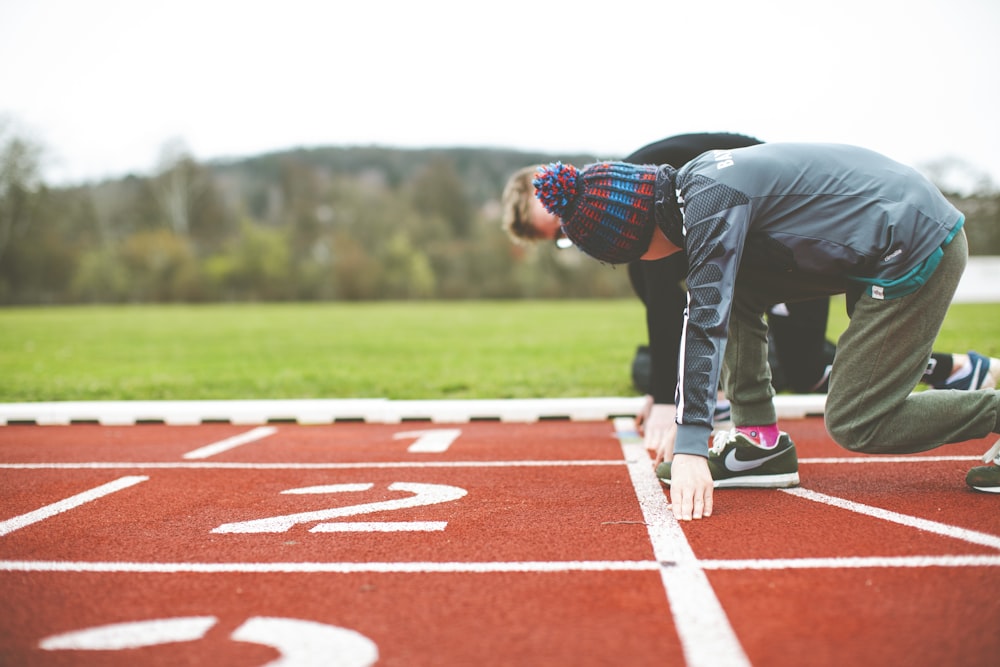 uomo in camicia a quadri nera e rossa e pantaloni neri in piedi sul campo di atletica durante il giorno