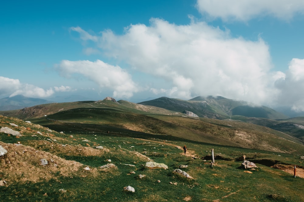 green grass field near mountain under white clouds and blue sky during daytime