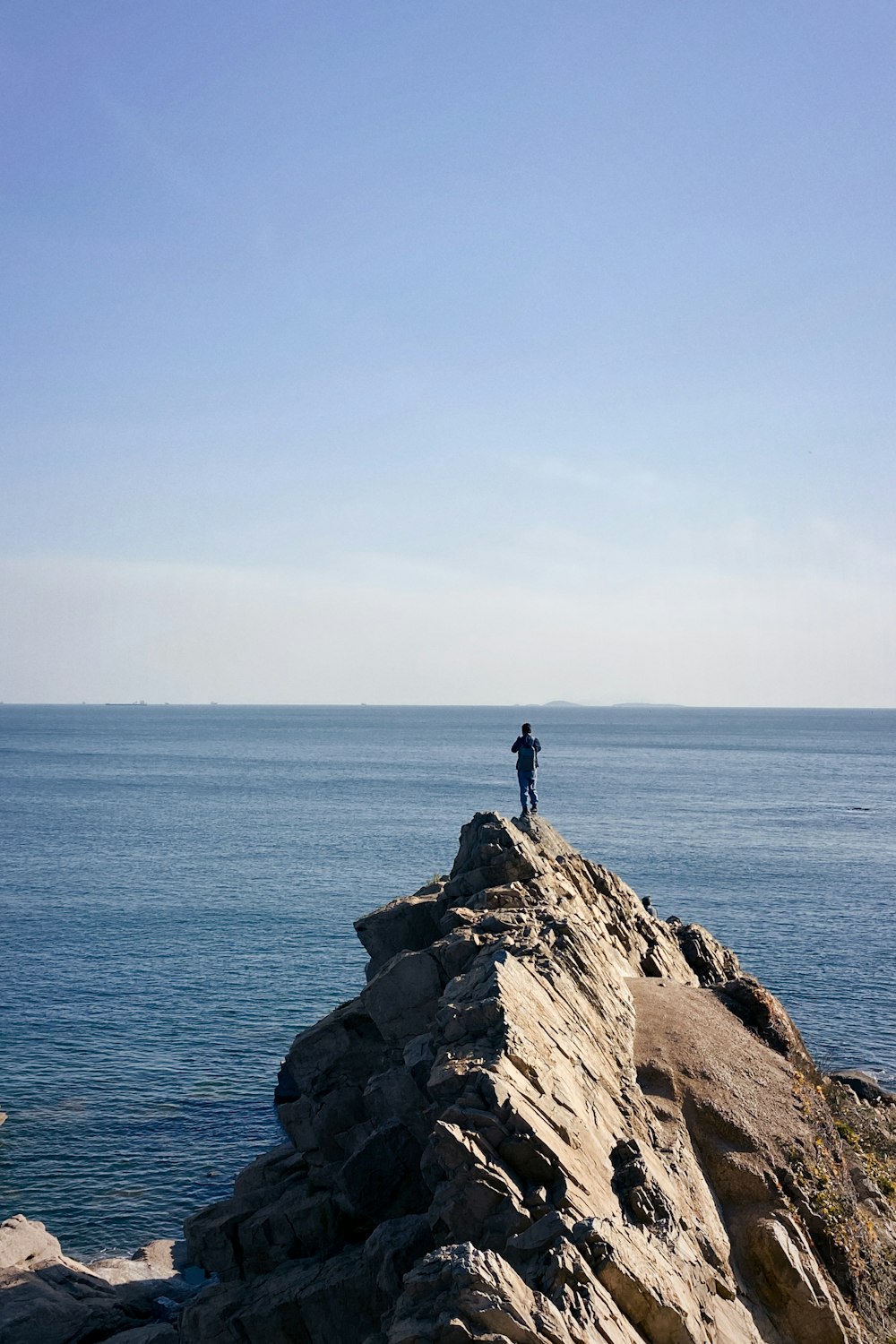man standing on rock formation near body of water during daytime