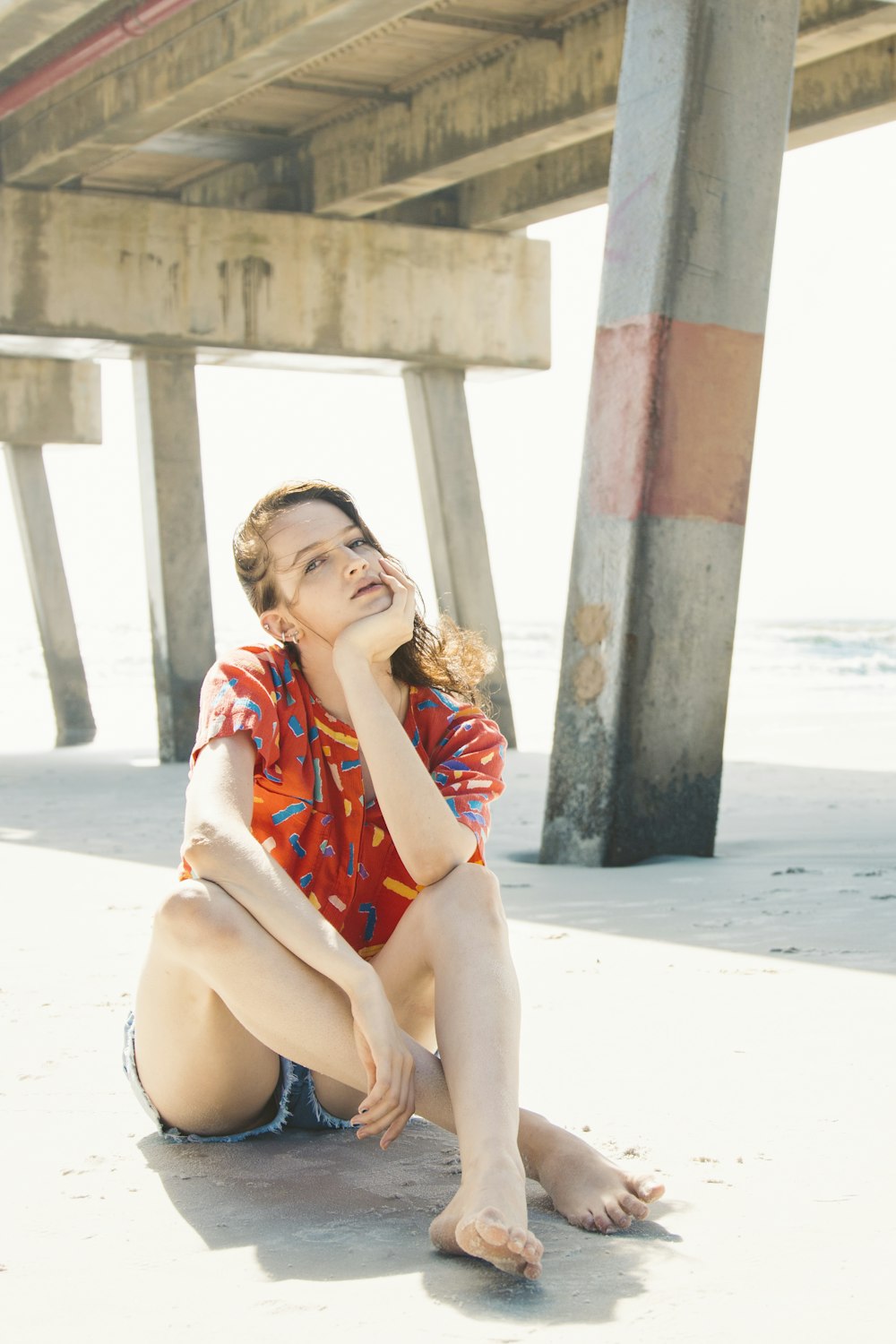woman in red and white floral dress sitting on white sand during daytime