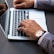 A person wearing a business suit types on a laptop keyboard. They have a wristwatch with a brown leather strap on their left wrist. The scene captures a professional setting, possibly in an office.