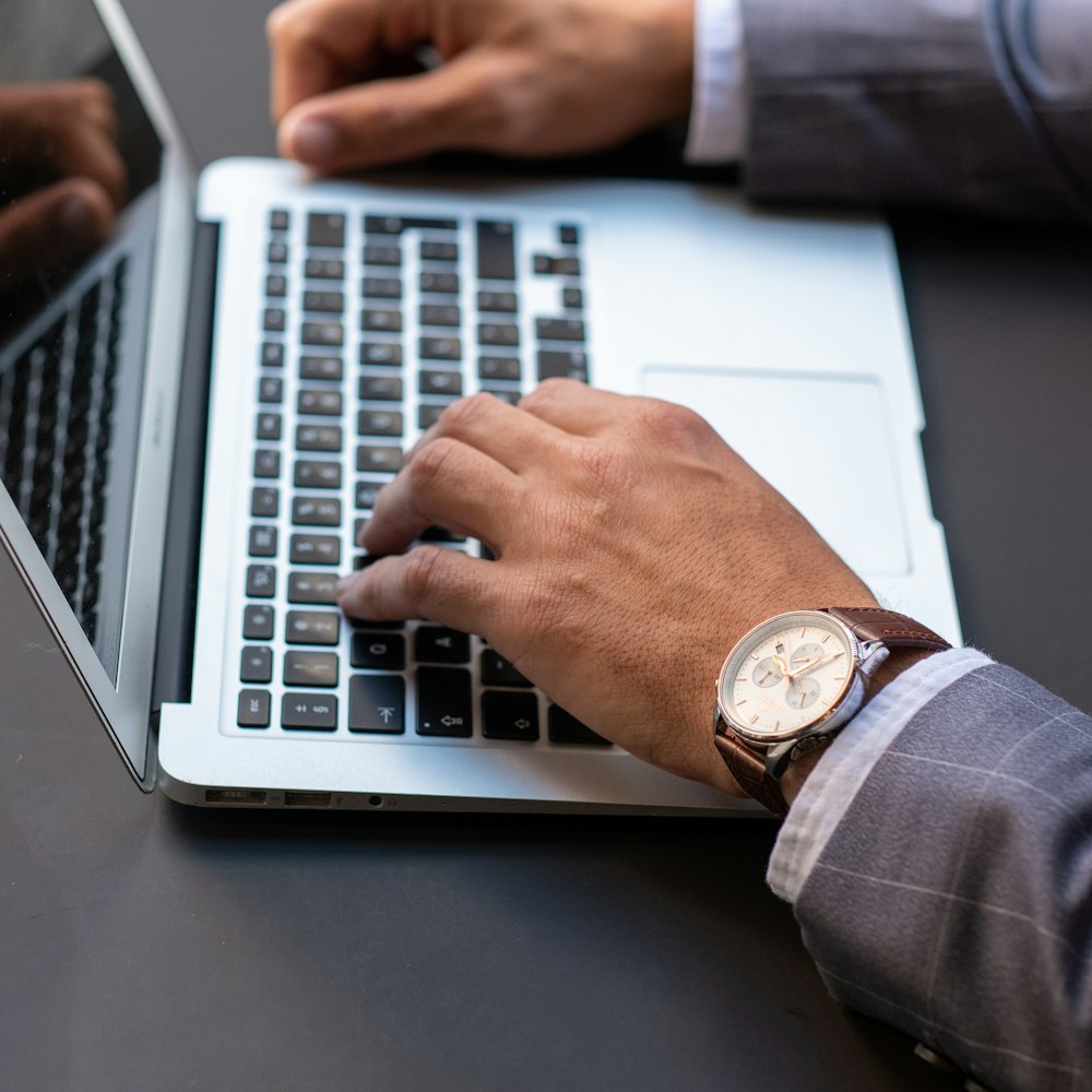 person wearing black leather strap gold round analog watch using macbook pro