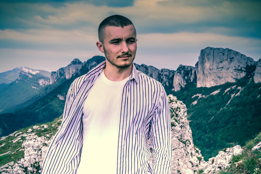 man in white and black striped long sleeve shirt standing on rocky mountain during daytime