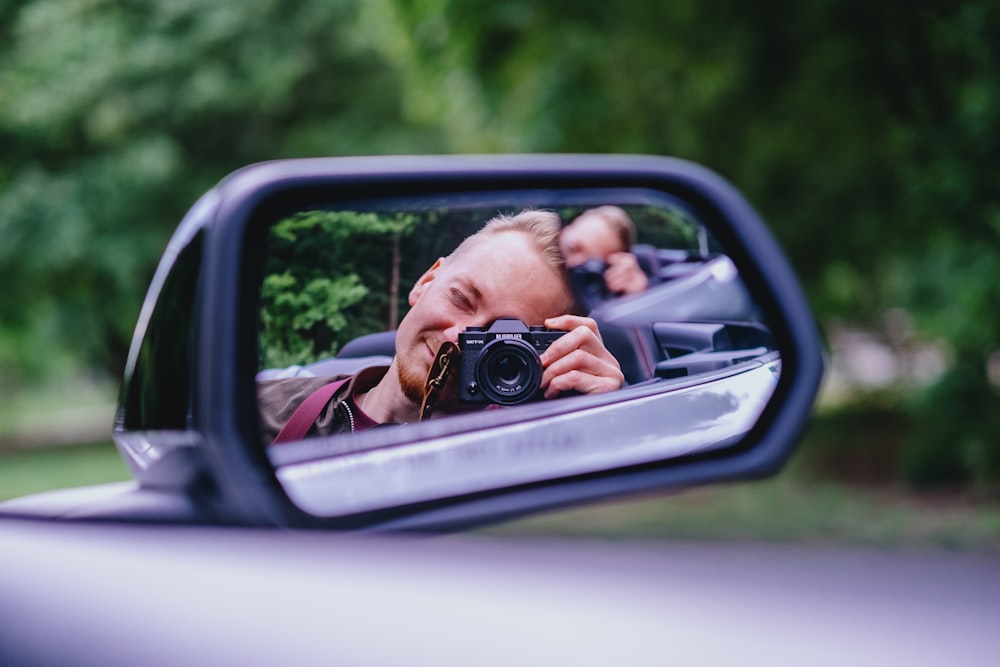 man in black shirt taking photo of car side mirror