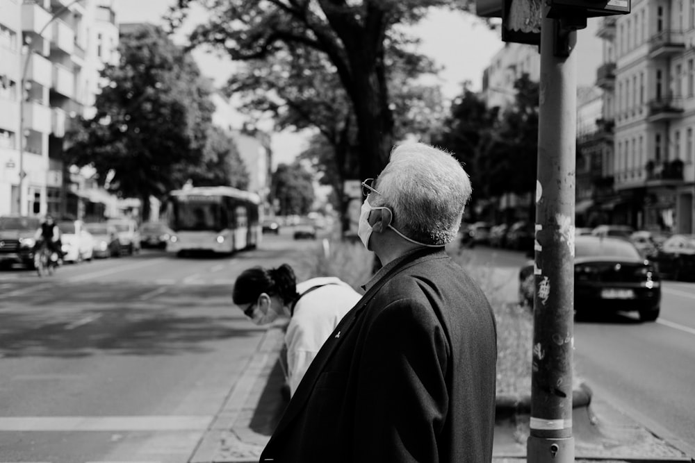 man in black suit standing on sidewalk in grayscale photography