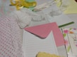 Various stationery items are laid out on a surface, including polka dot wrapping paper, a piece of white lace, a pink envelope, a sheet with floral design, and a yellow ribbon. There are also notepads, one with writing, and a card with a drawn bunny.