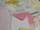 Various stationery items are laid out on a surface, including polka dot wrapping paper, a piece of white lace, a pink envelope, a sheet with floral design, and a yellow ribbon. There are also notepads, one with writing, and a card with a drawn bunny.