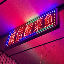 A vibrant LED sign glowing brightly outside a busy storefront at night.