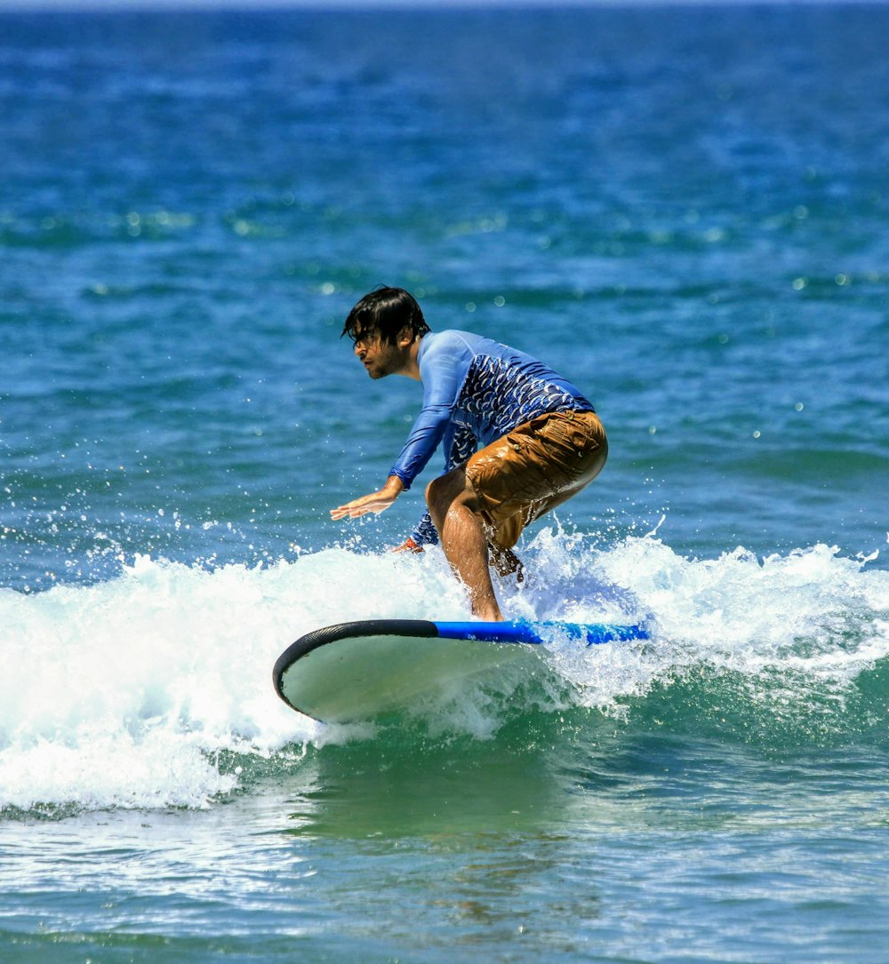 파란색 티셔츠와 노란색 반바지를 입은 남자가 낮에 바다에서 서핑을 하고 있습니다.