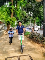 A person riding an electric scooter on a city street with greenery around.