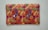 A rectangular fabric piece features intricate and colorful embroidery with floral and paisley patterns. The background is a rich orange shade, and the embroidery includes vibrant hues of purple, green, yellow, and pink with threads forming detailed and symmetrical designs.