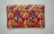 A rectangular fabric piece features intricate and colorful embroidery with floral and paisley patterns. The background is a rich orange shade, and the embroidery includes vibrant hues of purple, green, yellow, and pink with threads forming detailed and symmetrical designs.