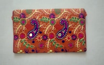 A rectangular fabric piece features intricate and colorful embroidery with floral and paisley patterns. The background is a rich orange shade, and the embroidery includes vibrant hues of purple, green, yellow, and pink with threads forming detailed and symmetrical designs.