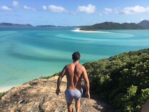 A traveler standing on a cliff edge overlooking turquoise ocean waves crashing on rocky shores.