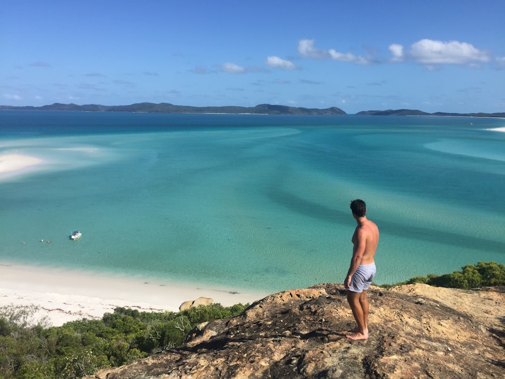 woman in white bikini standing on rock near body of water during daytime