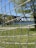A close-up of a net, with a grassy area and trees in the background. A large bridge is visible in the distance across a body of water.