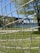 A close-up of a net, with a grassy area and trees in the background. A large bridge is visible in the distance across a body of water.