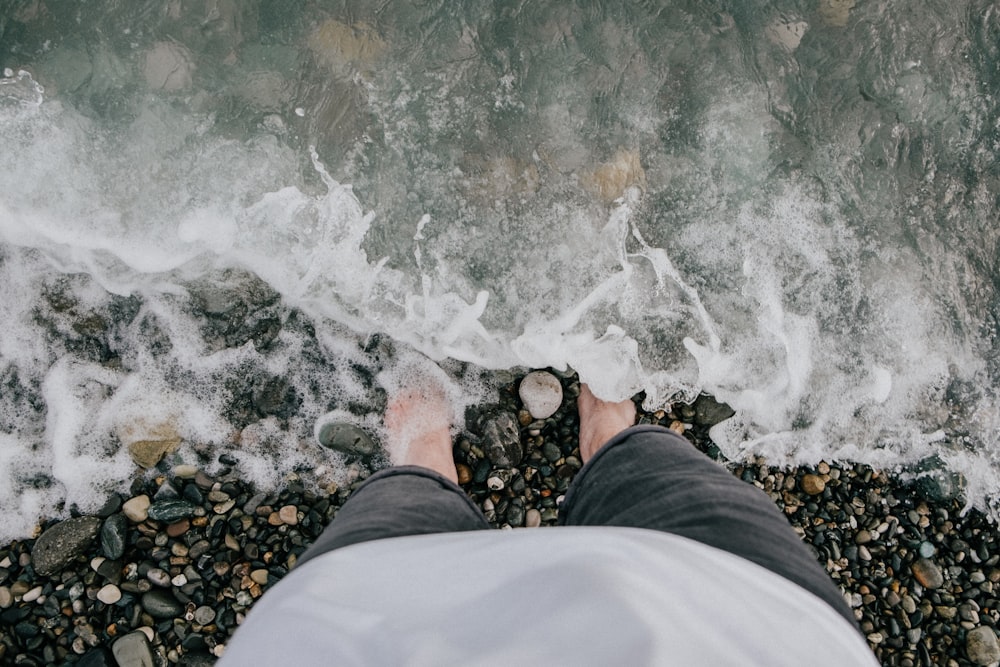 person in black pants and brown shoes standing on rocky shore