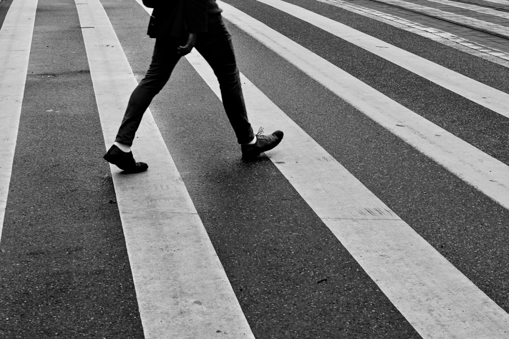 Person in schwarzen Hosen und schwarzen Turnschuhen, die auf der Fußgängerzone geht