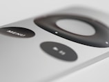 A close-up view of a sleek, silver remote control with a prominent black circular navigation button and a 'MENU' button. The design is minimalist and modern.