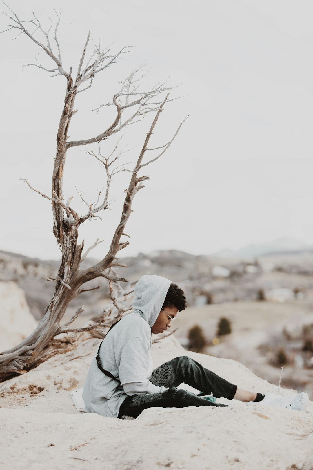 man in white hoodie sitting on brown sand during daytime