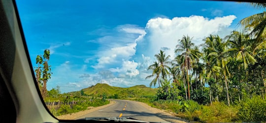 gray asphalt road between green grass field under blue and white cloudy sky during daytime in Seram Bagian Barat Indonesia