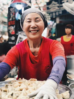 A smiling local woman serving piping hot Dohneiiong, a pork dish cooked with black sesame seeds.