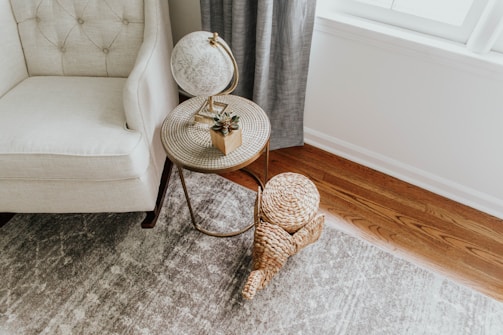 A cozy corner featuring a boho rattan accent chair beside a wooden nesting table with a terracotta planter on top.