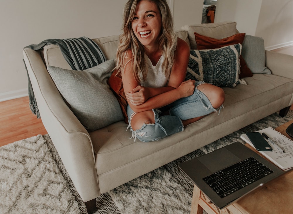 woman in gray tank top and blue denim jeans sitting on gray sofa