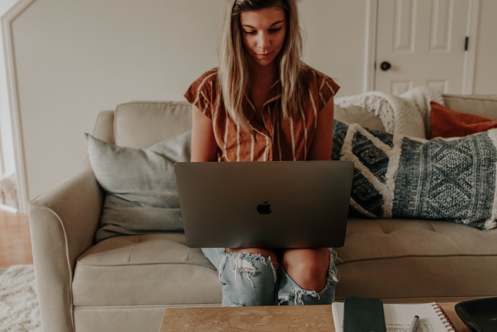 woman in brown long sleeve shirt sitting on white couch using macbook