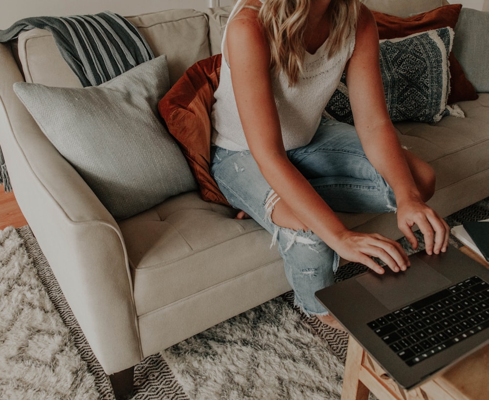 woman in gray tank top and blue denim jeans sitting on gray couch