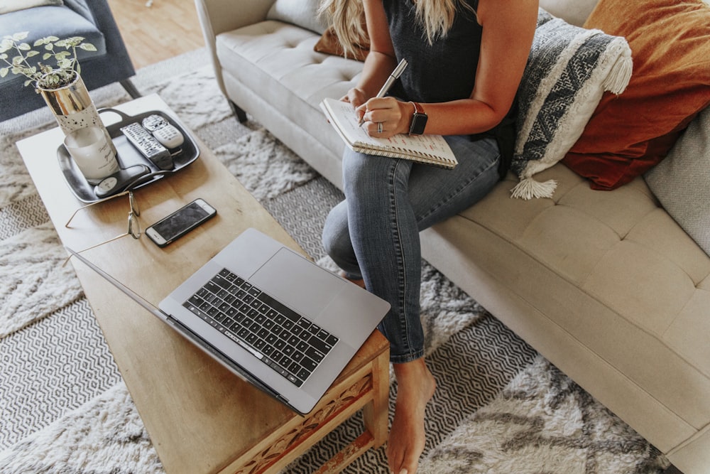 woman in black and white tank top and blue denim jeans sitting on white couch