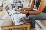 woman in black tank top and blue denim jeans sitting on chair using macbook pro