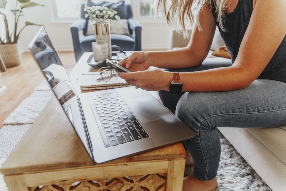woman in black tank top and blue denim jeans sitting on chair using macbook pro