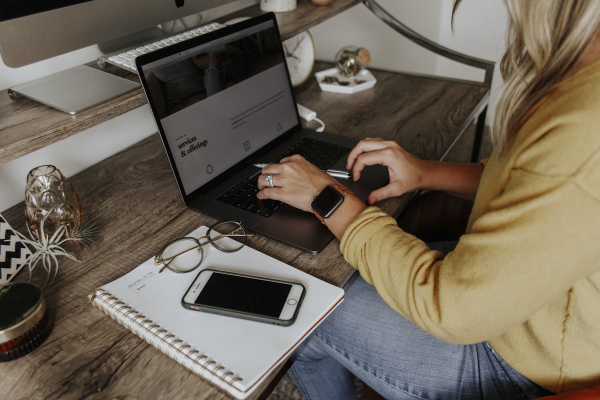 Dirigeante au travail sur son ordinateur, carnet de notes et smartphone à côté, en session de réflexion sur son activité commerciale