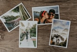 Four photographs are arranged on a wooden surface. One photo shows a close-up of palm leaves, another features a couple smiling with one person kissing the other on the cheek, a third depicts a woman walking with a child along a path lined with tropical plants, and the fourth captures a scenic view of palm trees against a partly cloudy sky.