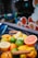 A colorful assortment of citrus fruits including lemons, limes, oranges, and grapefruits displayed in a wire basket. The background features a decorative window with pictures of sliced citrus fruits, creating a vibrant and fresh setting.
