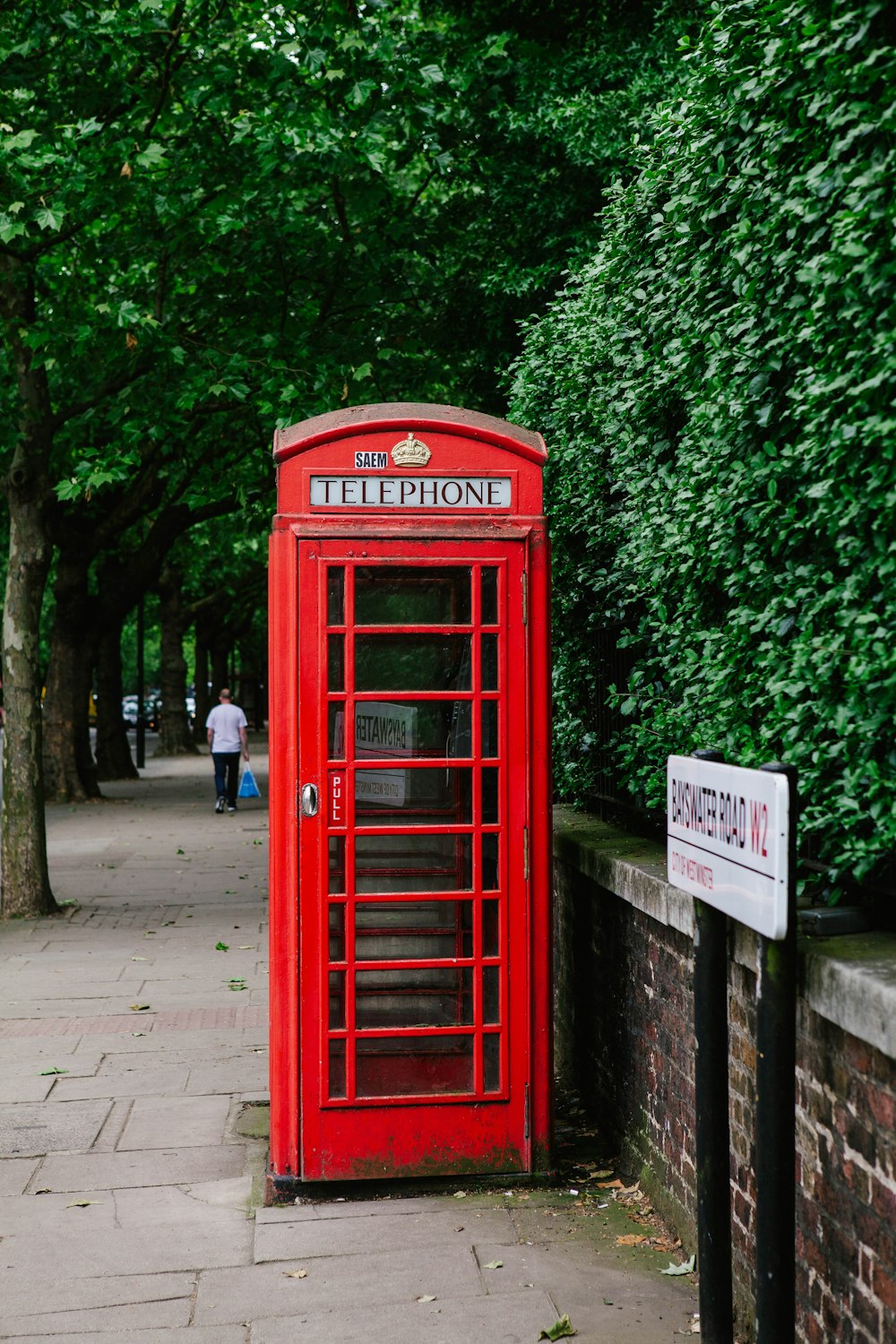 red telephone booth near green trees during daytime