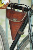 A sleek black crossbody bag hanging from a vintage bicycle handle.