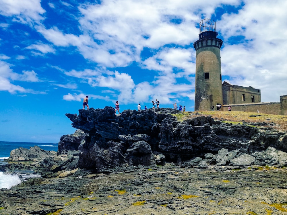 Faro marrón y blanco en la colina rocosa bajo el cielo nublado azul y blanco durante el día