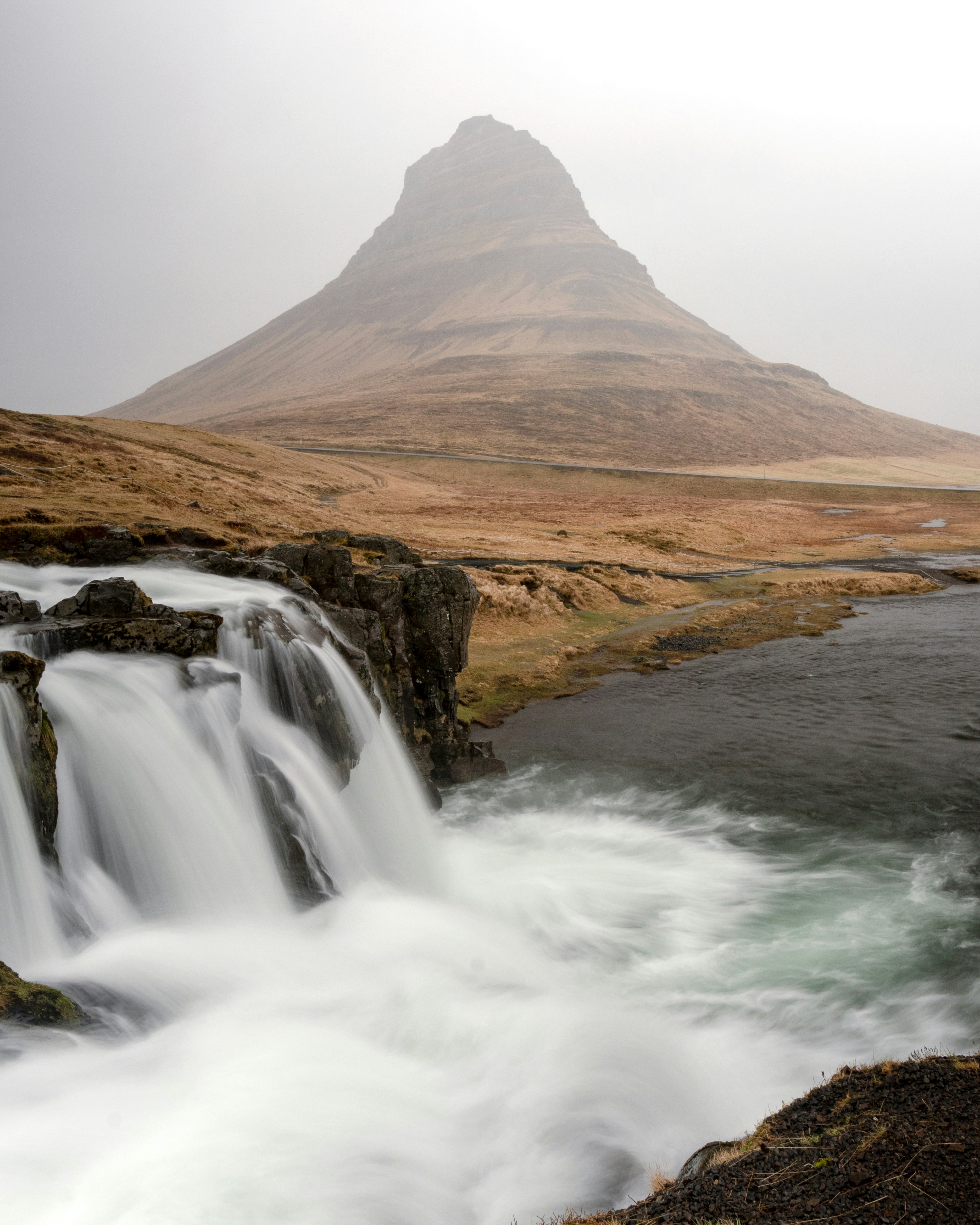 waterfalls near brown mountain under white sky during daytime