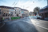 A group of protesters is gathered on a city street holding large banners. The banners contain messages about environmental issues and non-violence. The scene is set in an urban area with buildings, signs, and vehicles visible. The sky is clear with some light from the sun illuminating the street.