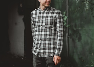 man in blue and white plaid dress shirt standing beside green wall