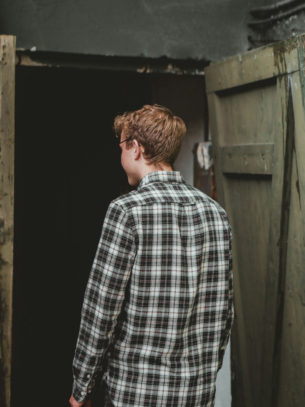 man in black and white plaid dress shirt standing near brown wooden door