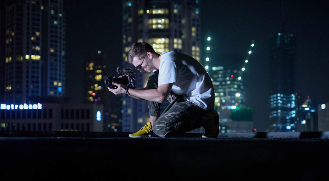 man in white t-shirt and black pants holding black dslr camera