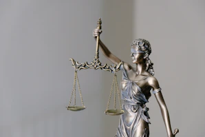 Statue of Lady Justice holding scales with a blurred courthouse in the background.